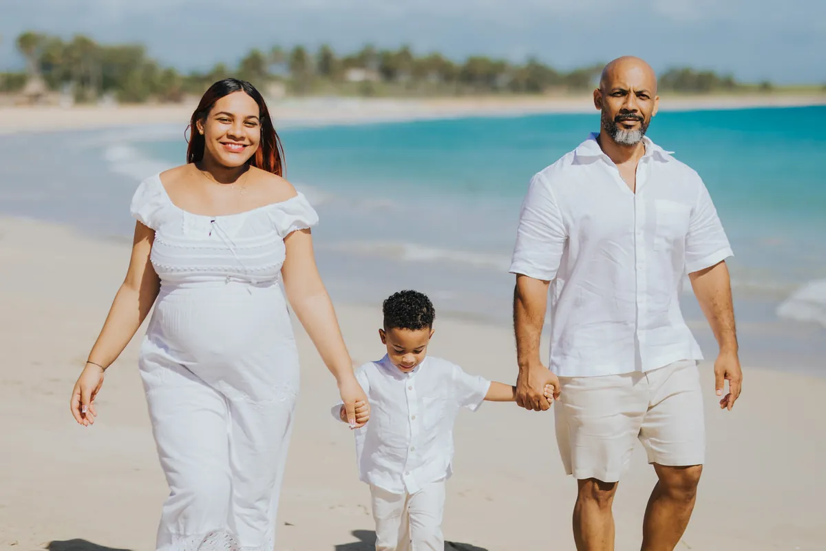 Family walking hand in hand along the shore, mom expecting
