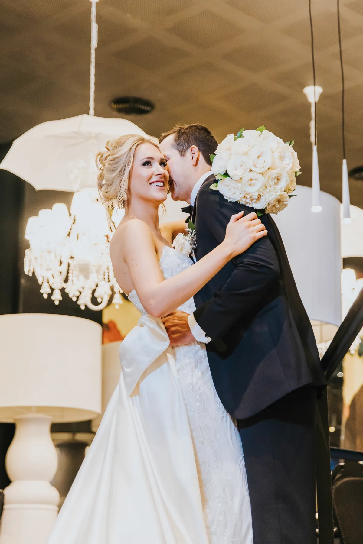 Groom whispering to the laughing bride under white lamps